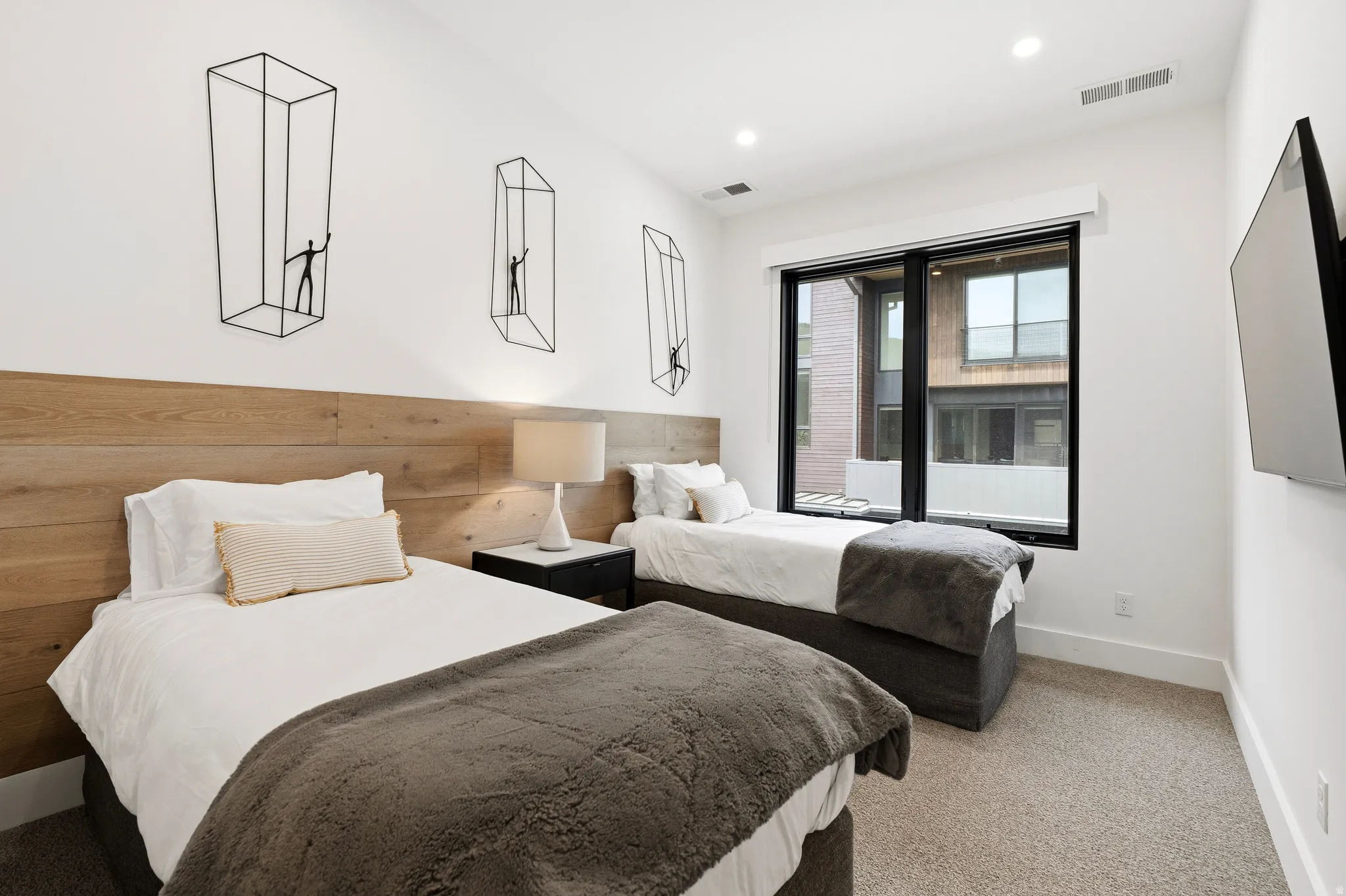 Spacious room featuring wood-finish accent wall, large window with black trim, recessed lighting, and light-toned carpet flooring