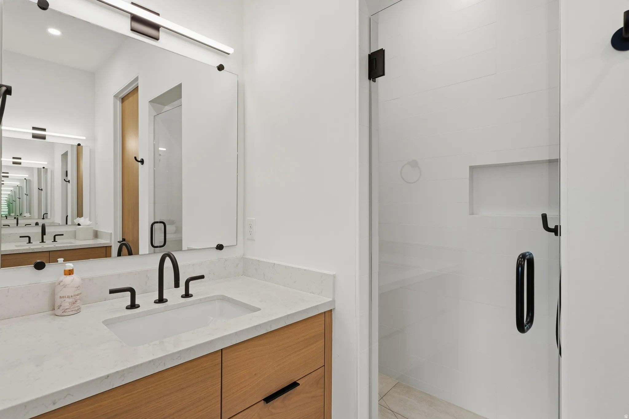 Contemporary bathroom featuring a light wood-finish vanity with drawer storage, a white countertop with an integrated rectangular sink, and matte black fixtures