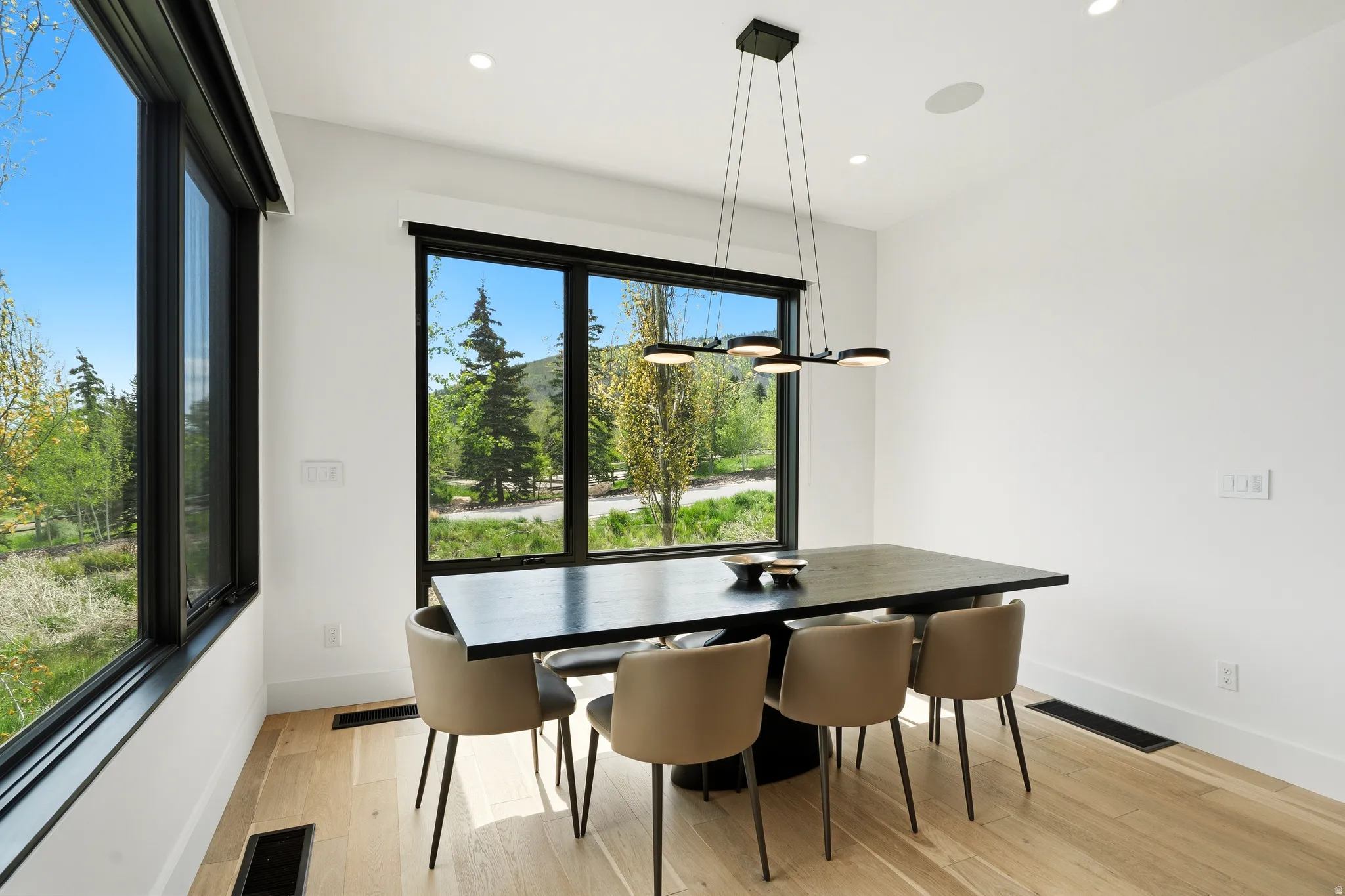 Dining area featuring large black-framed windows, a contemporary linear chandelier, recessed lighting, and wood-finish flooring