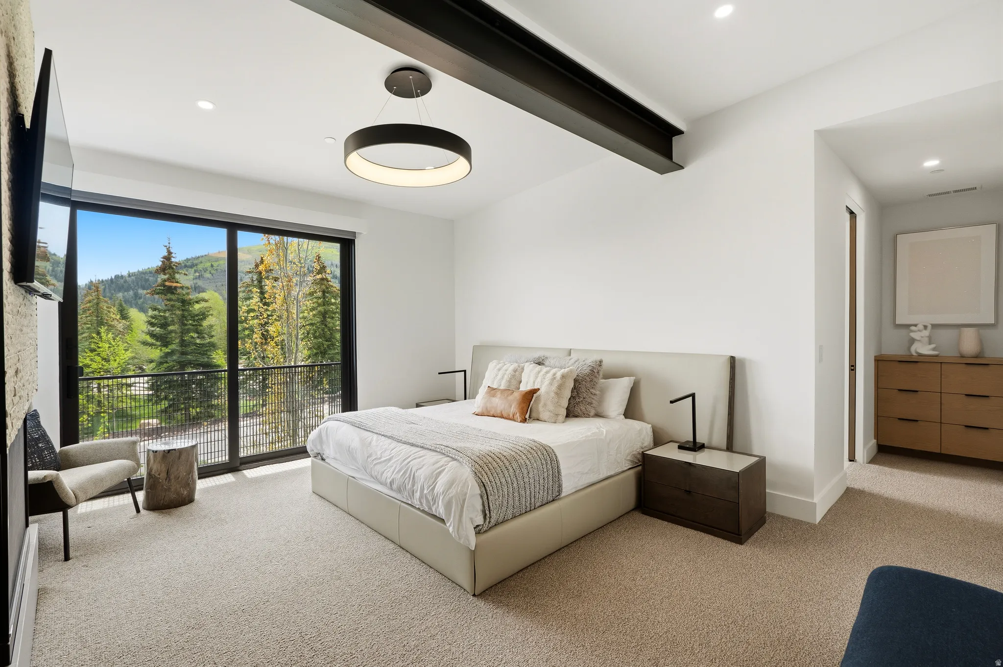 Spacious room featuring a floor-to-ceiling glass sliding door, leading to a private balcony with mountain and tree scenery