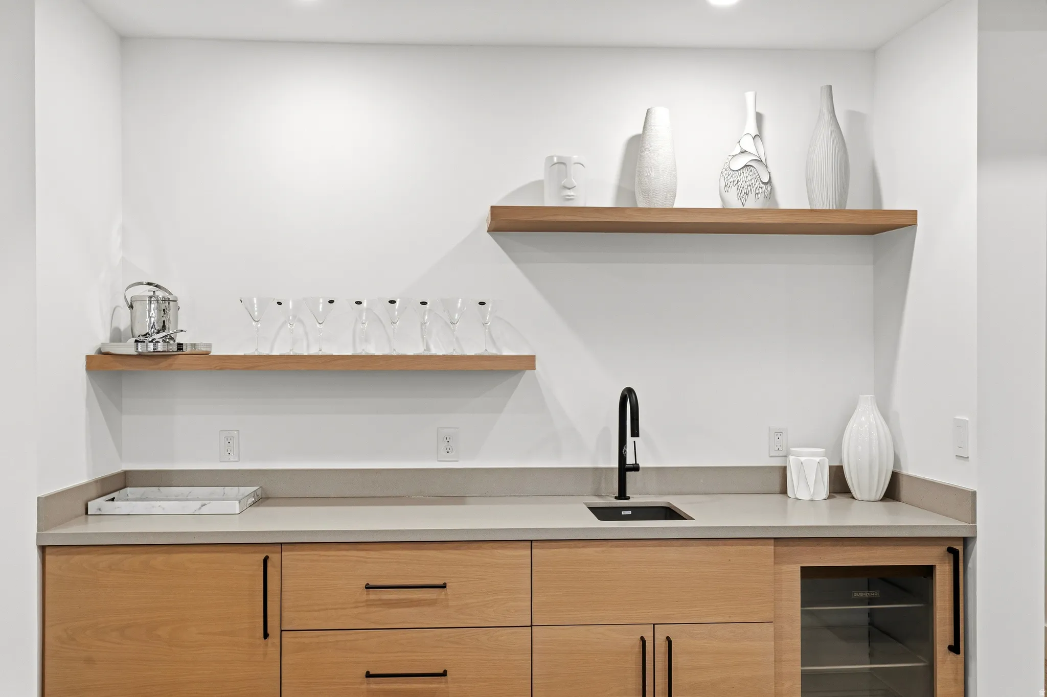 Modern wet bar featuring natural wood-finish cabinetry, a light-toned countertop, and a built-in beverage cooler