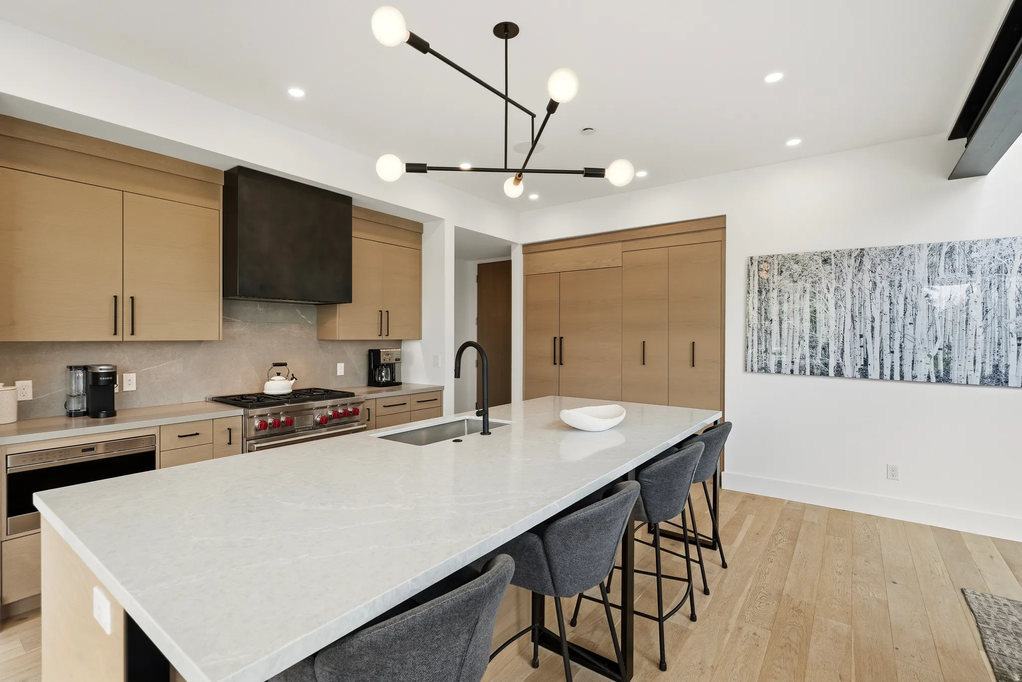 Gourmet kitchen featuring a substantial island with seating, a professional-grade range, custom light wood-finish cabinetry, a large built-in refrigerator, and light wood-finish flooring
