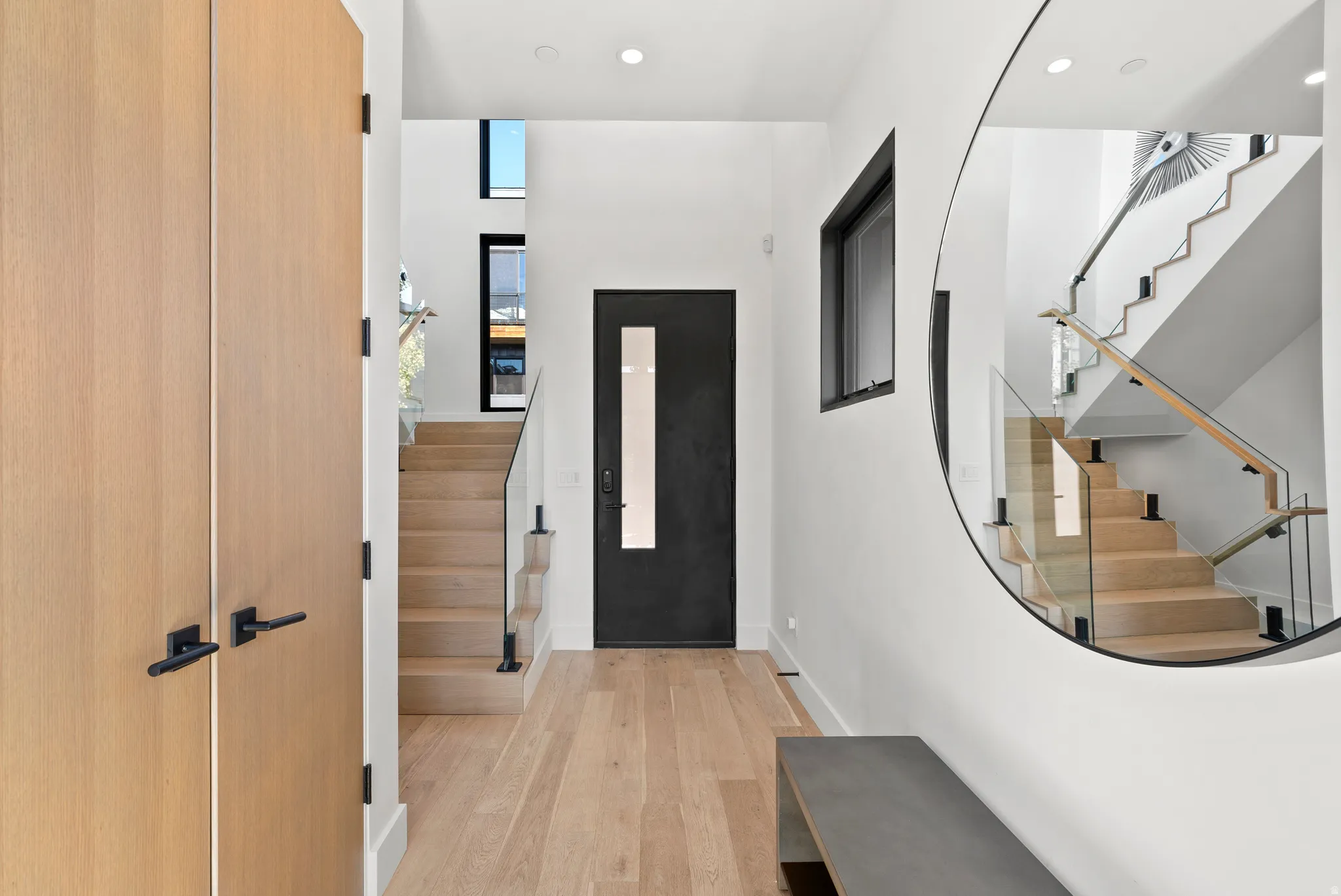 Entryway featuring wood-finish flooring, a contemporary staircase with glass railings and wood handrails, and a solid core entry door with vertical glass insert.