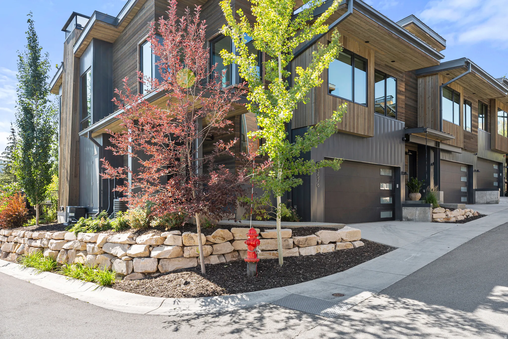 Modern multi-level townhome featuring dark wood-look siding, corrugated metal accents, and a stone retaining wall
