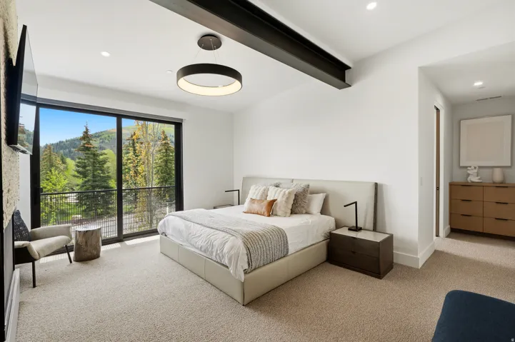 Spacious room featuring a floor-to-ceiling glass sliding door, leading to a private balcony with mountain and tree scenery