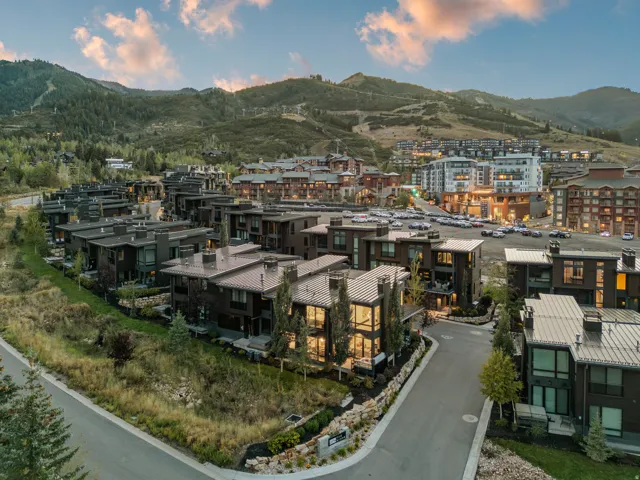 Modern architectural design in a community setting, featuring pitched metal roofs, extensive window placements, and a mountainous backdrop