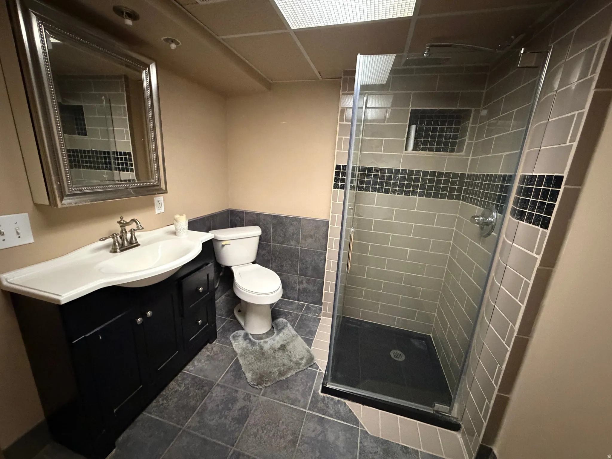 Bathroom featuring a glass-enclosed shower with subway tile and mosaic accents, a built-in shower niche, and a dark wood-finish vanity with an integrated sink