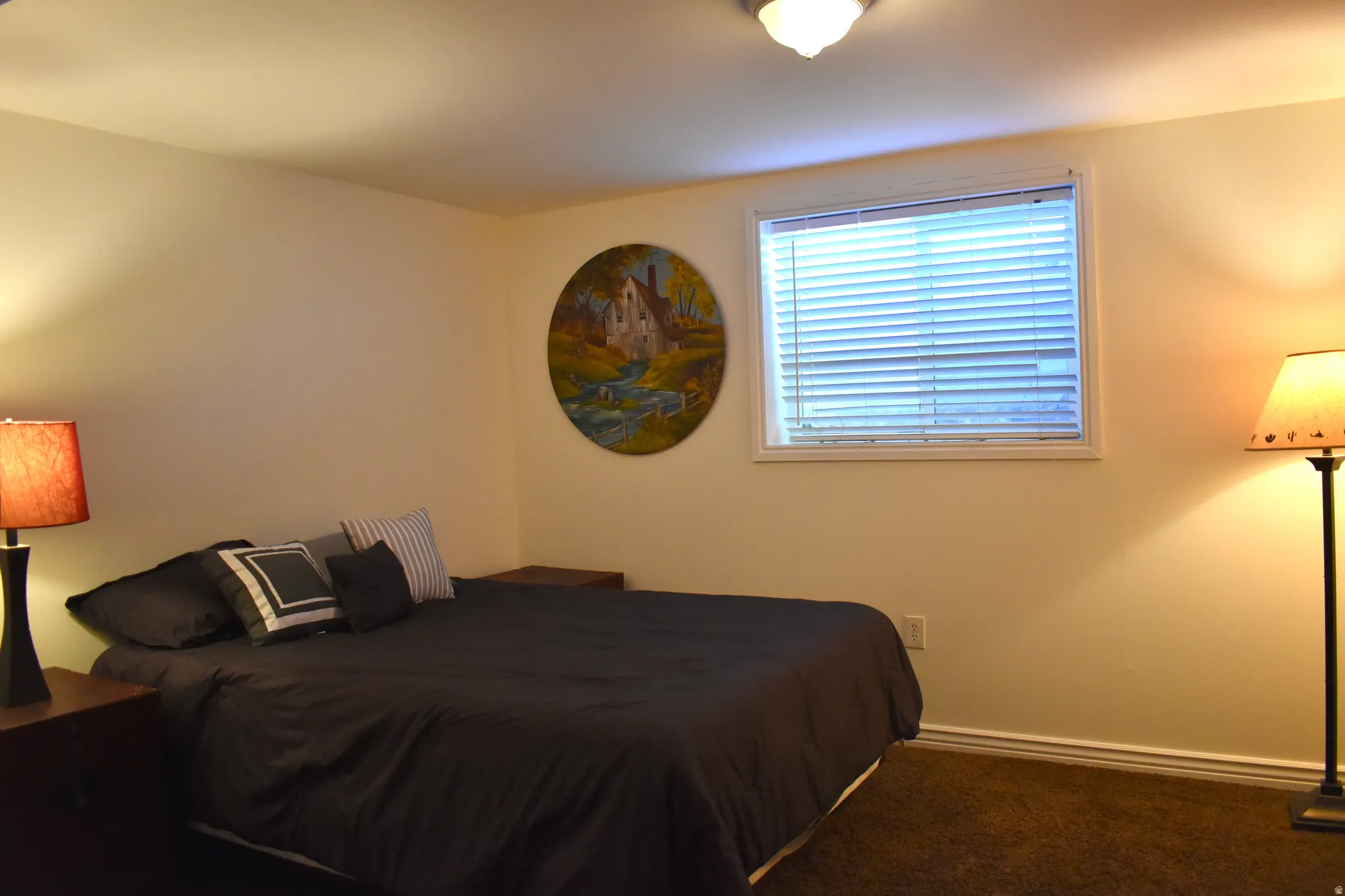 Carpeted bedroom featuring a large window with horizontal blinds, neutral wall paint, and a built-in ceiling light fixture
