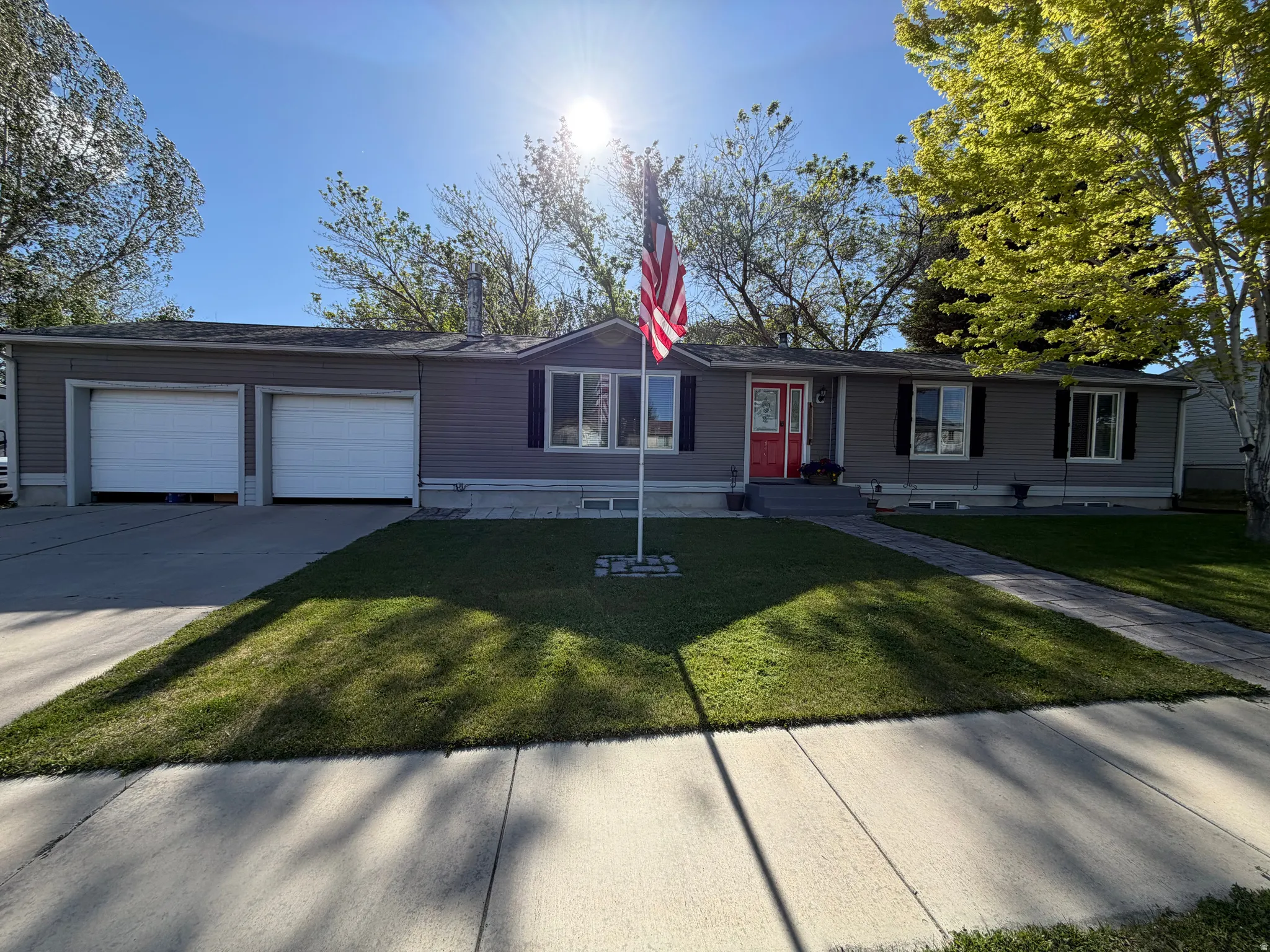 Ranch-style residence featuring grey siding, a red entry door, and a two-car attached garage with white doors