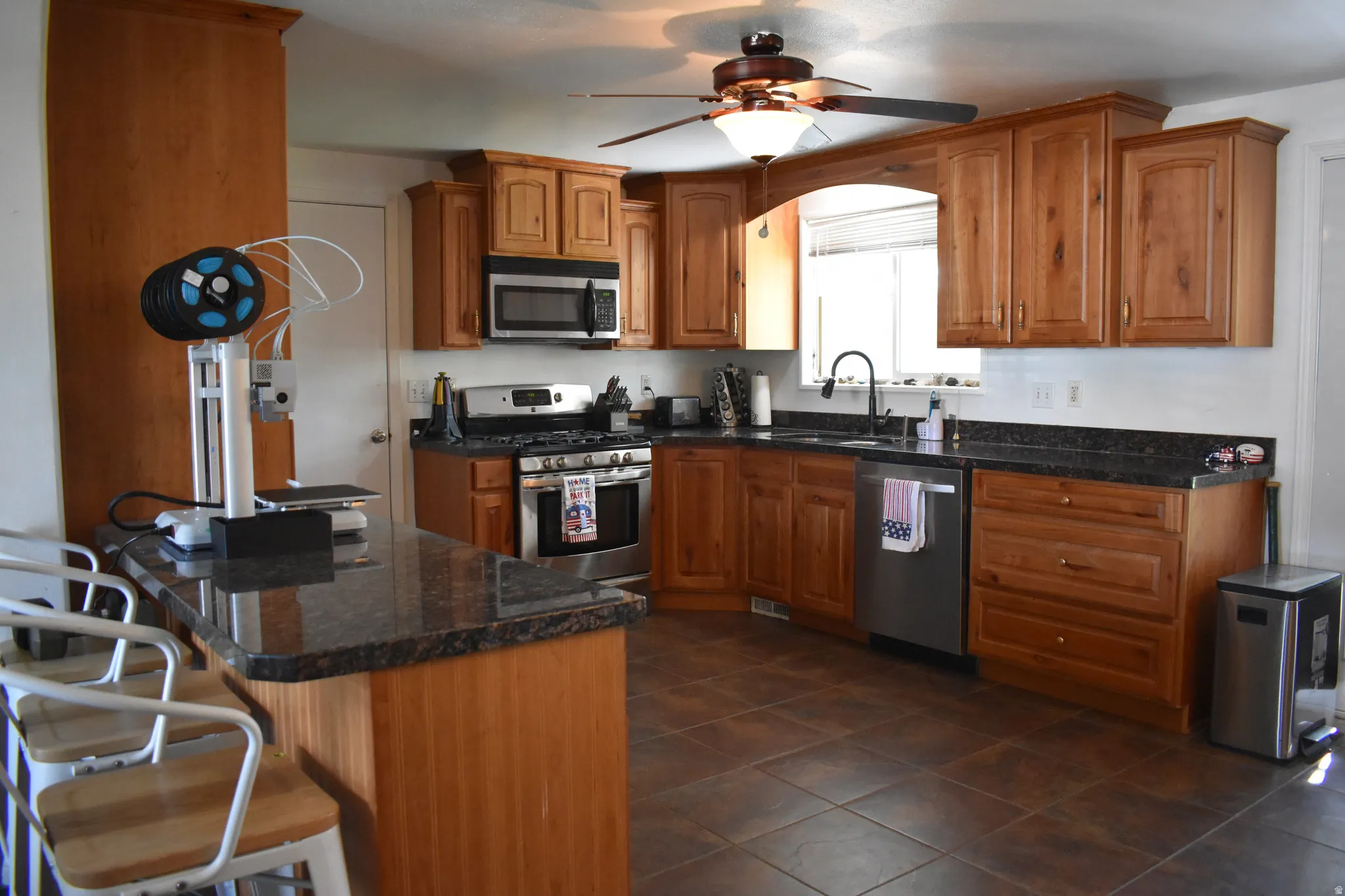 Kitchen featuring wood cabinetry, stainless steel appliances, dark stone countertops, an island with seating, and tile flooring