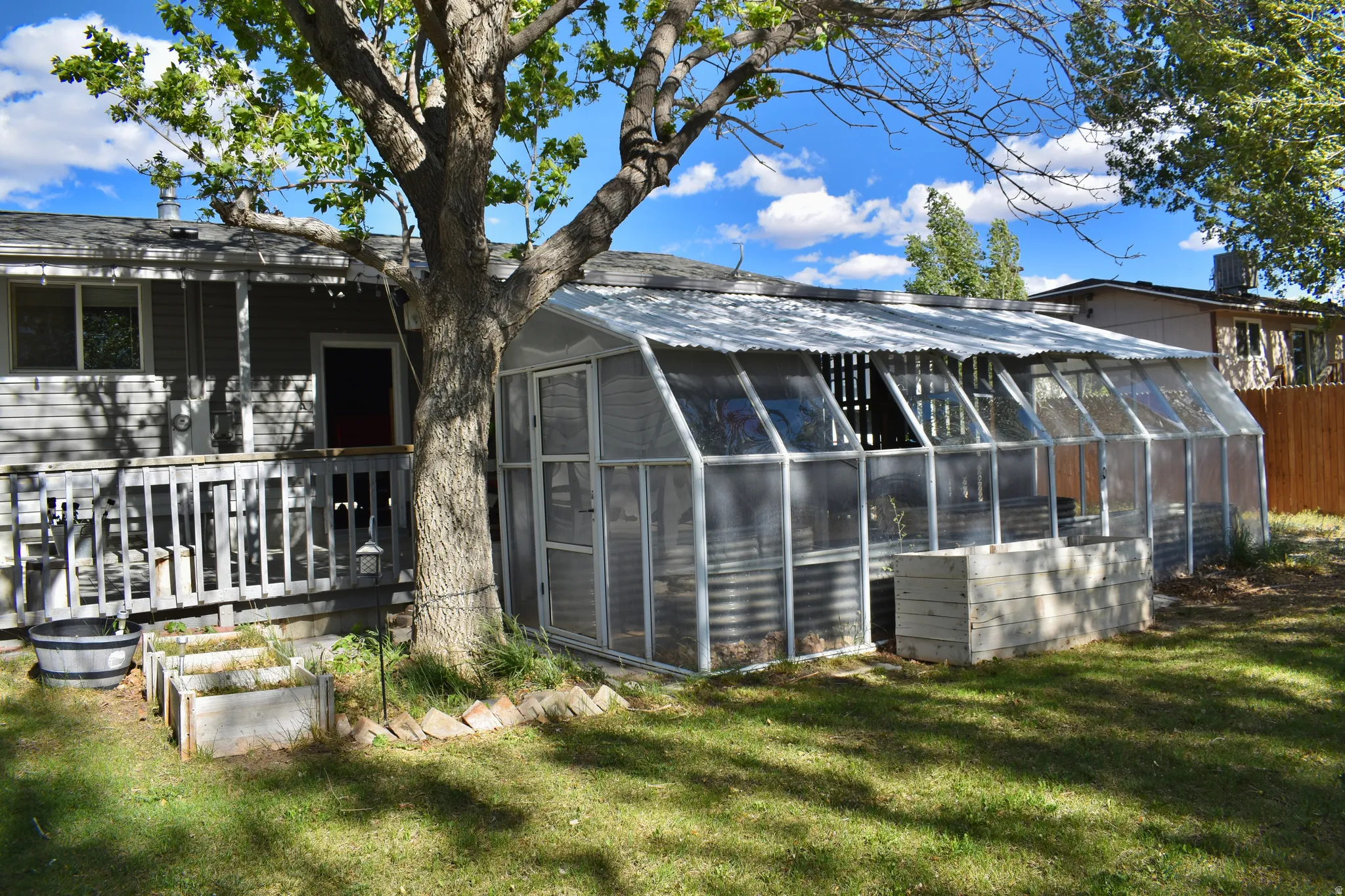 Rear exterior featuring an attached greenhouse, wood deck, and multiple raised garden beds