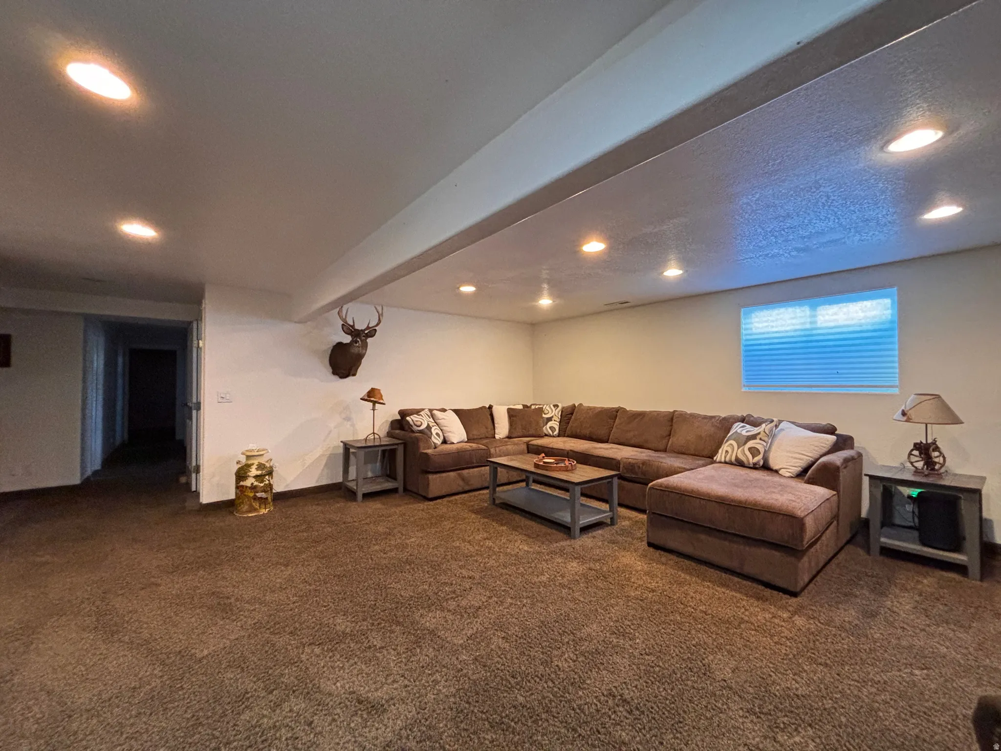 Spacious carpeted room featuring recessed ceiling lighting, a window with horizontal blinds, and a wide entryway