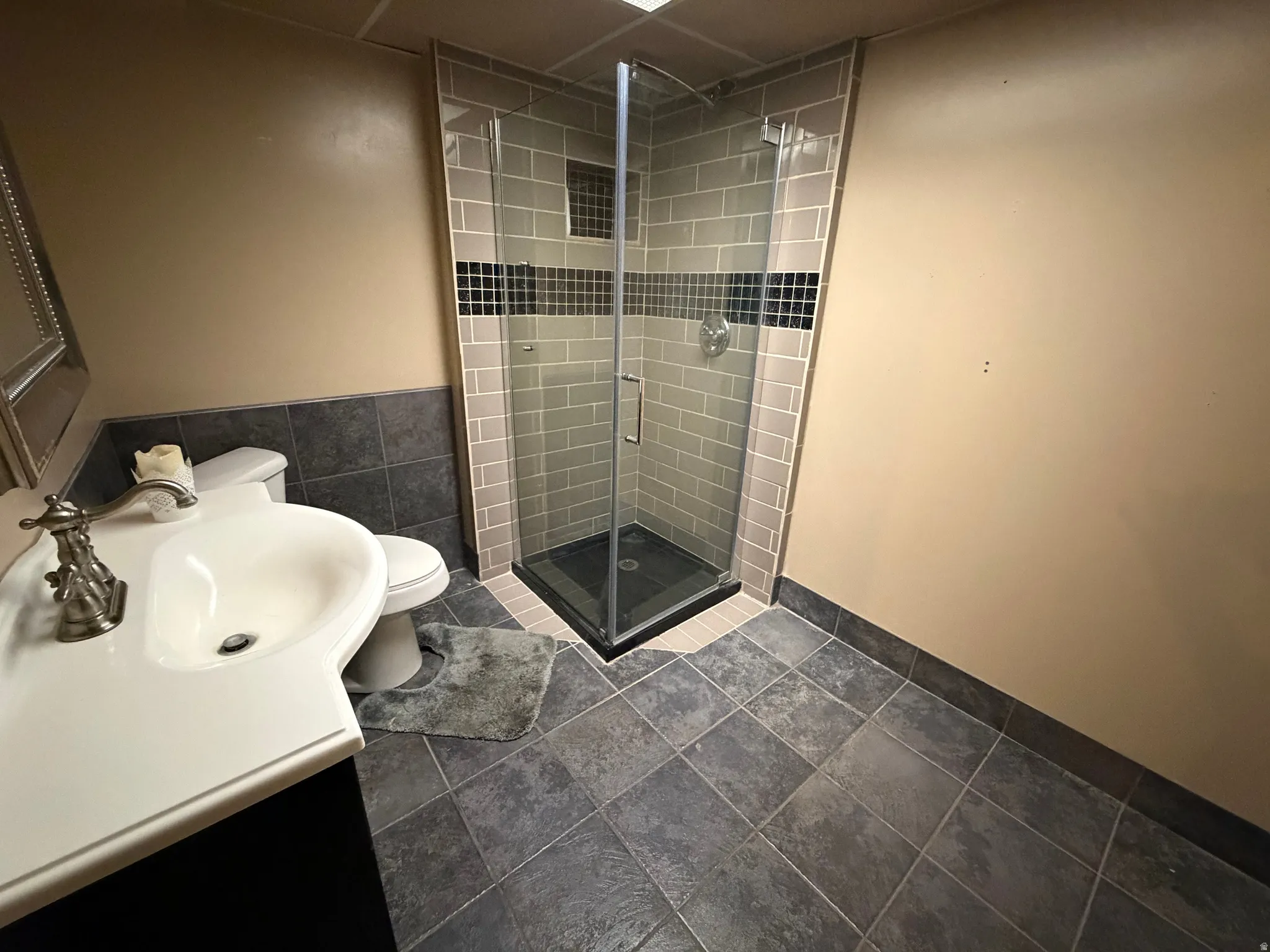 Corner glass shower enclosure with gray subway tile surround and a dark accent tile band