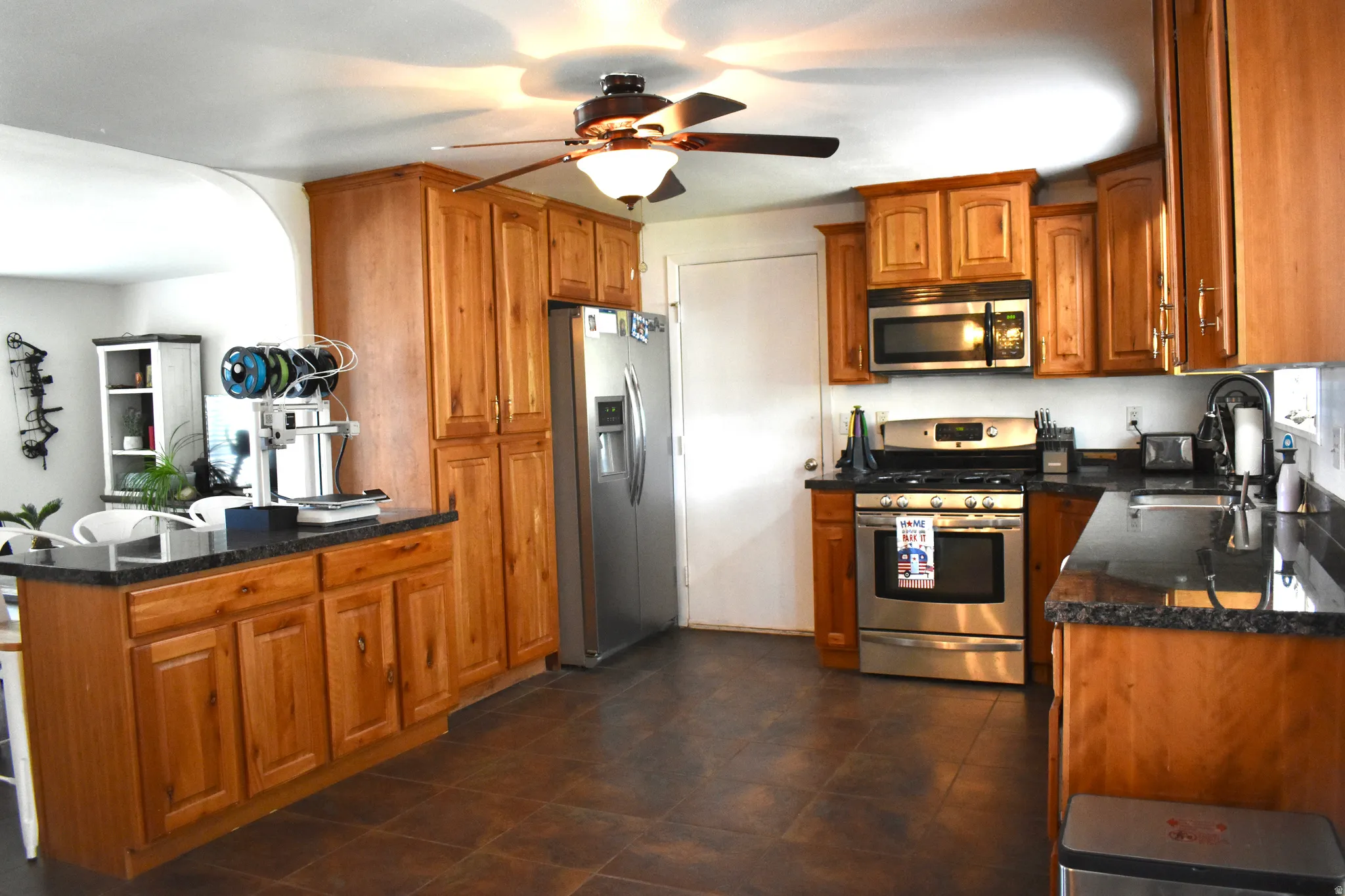 Spacious kitchen featuring warm-toned cabinetry, dark countertops, stainless steel appliances, and tile flooring