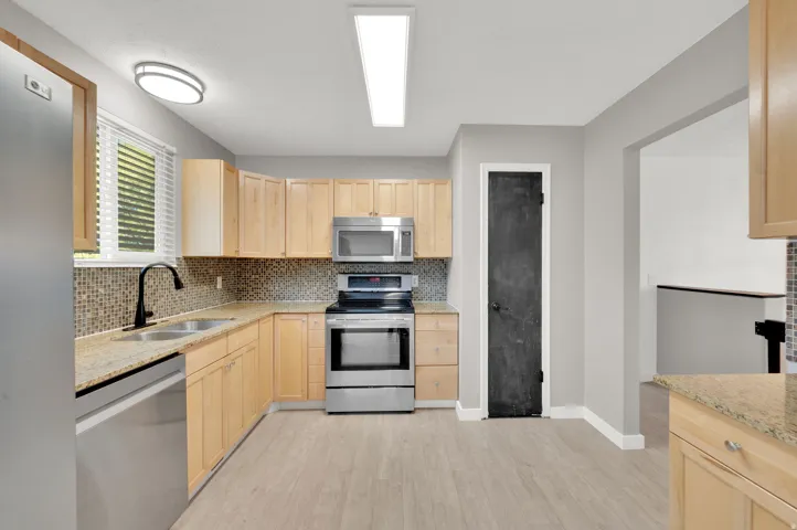 Kitchen featuring stainless steel appliances, light wood cabinetry, stone countertops, and a mosaic tile backsplash
