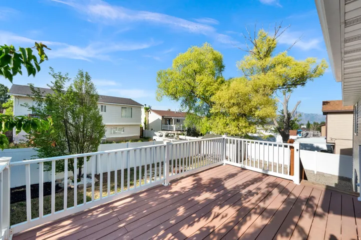 Expansive wood-finish deck with white railing, featuring a large tree and bright blue sky