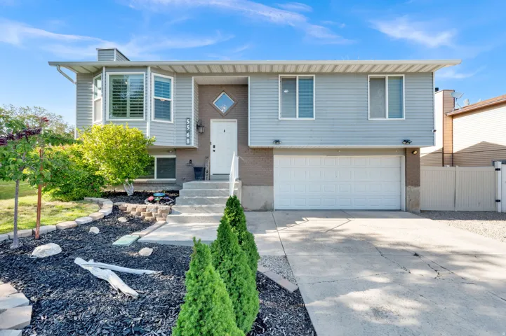 Split-level exterior featuring light gray siding with brick accents, an integrated two-car garage, and a concrete driveway