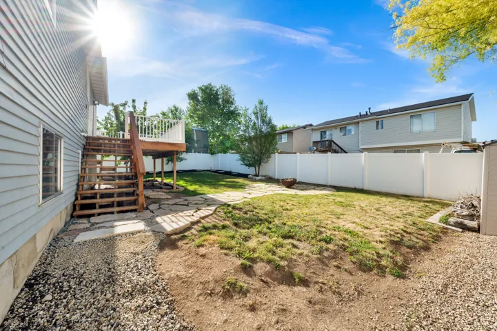 Rear exterior featuring a wood-tone deck with white railing, stone paver patio, partial privacy fencing, and a gravel perimeter