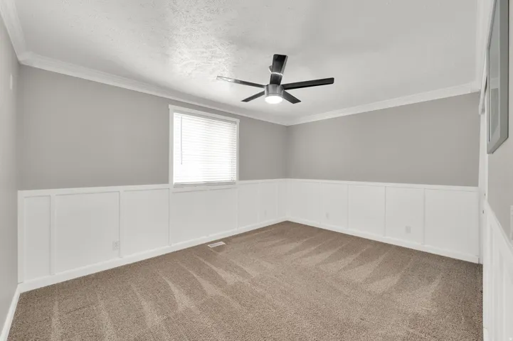 Room featuring light gray walls with white wainscoting, brown carpet, and a modern ceiling fan with integrated lighting