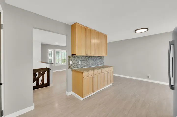 Kitchenette with natural wood-finish cabinetry, granite-style countertop, and mosaic tile backsplash
