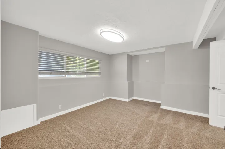 Room featuring neutral wall paint, light brown carpet flooring, a horizontal window with blinds, a flush-mount ceiling light fixture, and white baseboards