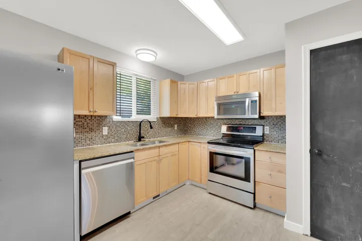 Kitchen featuring stainless steel appliances, wood cabinetry, granite countertops, mosaic tile backsplash, and light wood-finish flooring
