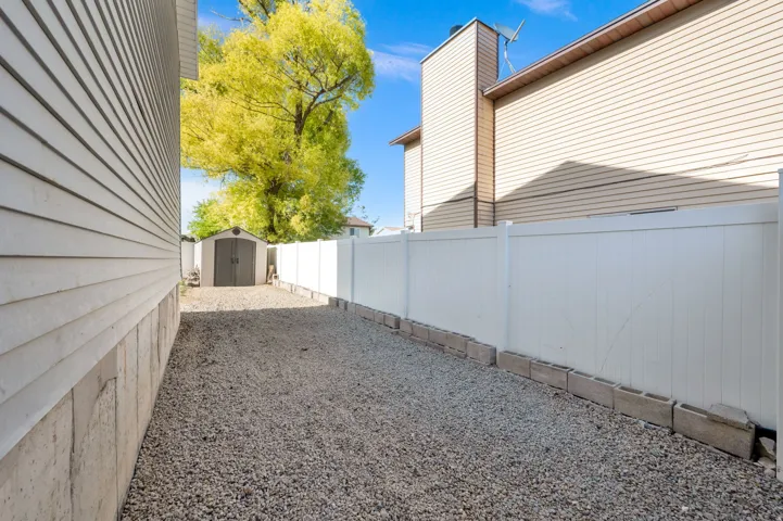 Gravel side yard featuring a storage shed and white privacy fencing