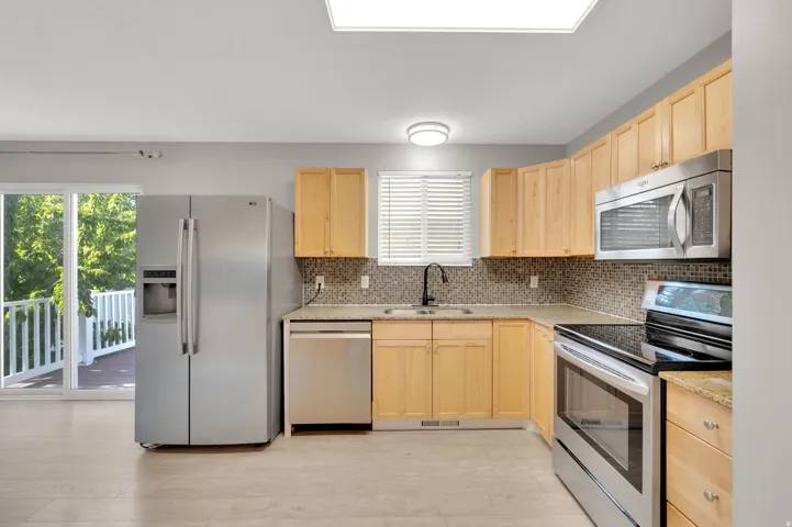 Well-appointed kitchen featuring wood-finish cabinetry, stainless steel appliances, granite countertops, and a mosaic tile backsplash