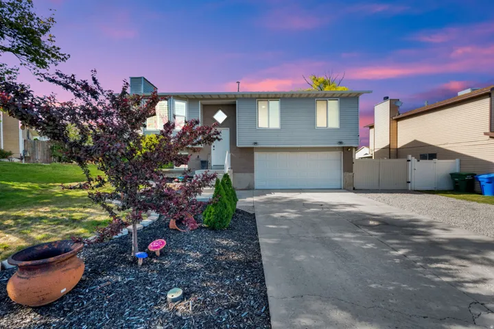 Split-level residence featuring a two-car garage, concrete driveway, and a gravel side parking area