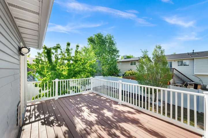 Expansive outdoor deck featuring composite wood flooring, white railing, and exterior wall light fixture