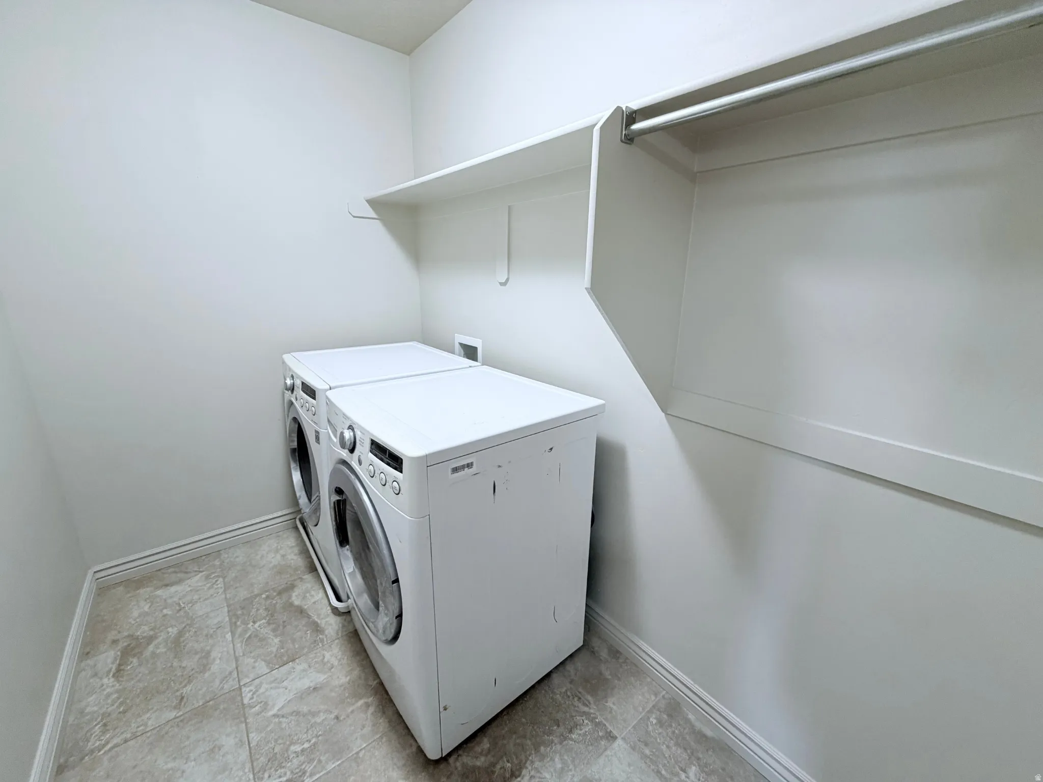 Dedicated laundry area featuring a front-loading washer and dryer set, tile flooring, built-in shelving, and a hanging rod for convenience