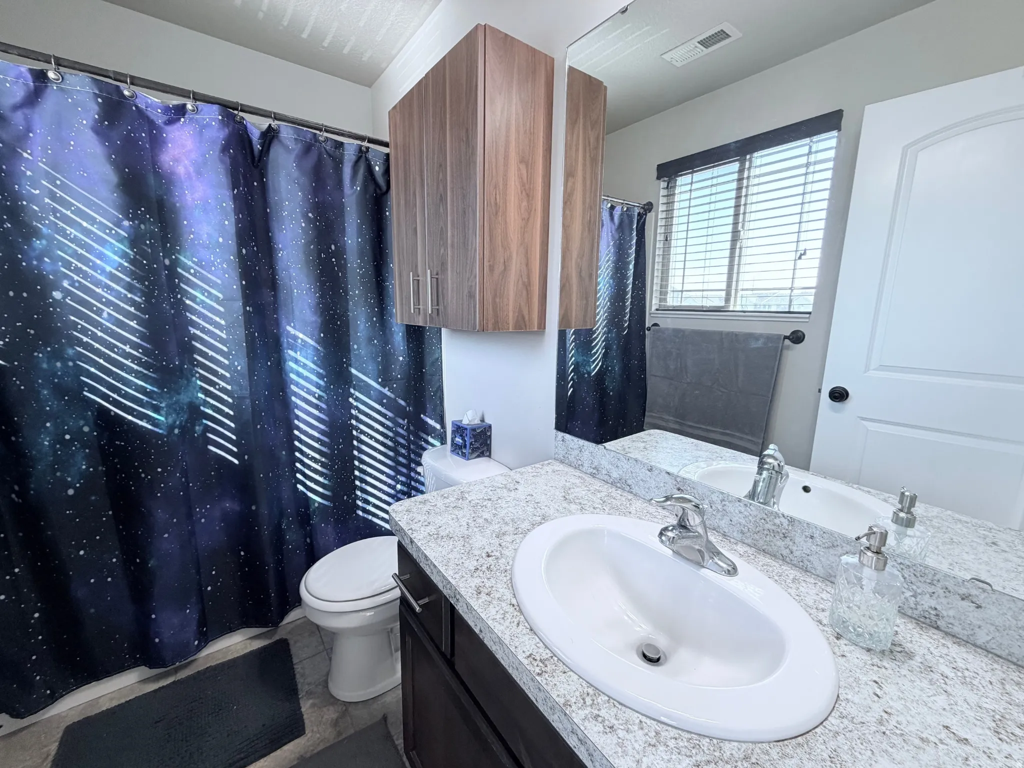 En-suite bathroom featuring a single vanity with an integrated sink, a light speckled countertop, and dark wood-finish cabinetry