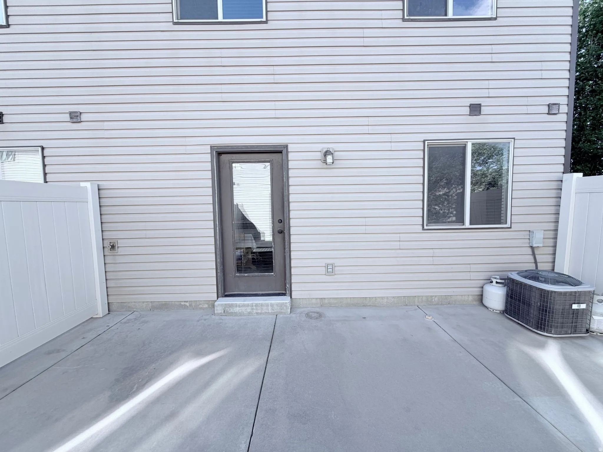 Rear exterior featuring a concrete patio with vinyl privacy fencing, a glass-paneled exterior door and central air unit