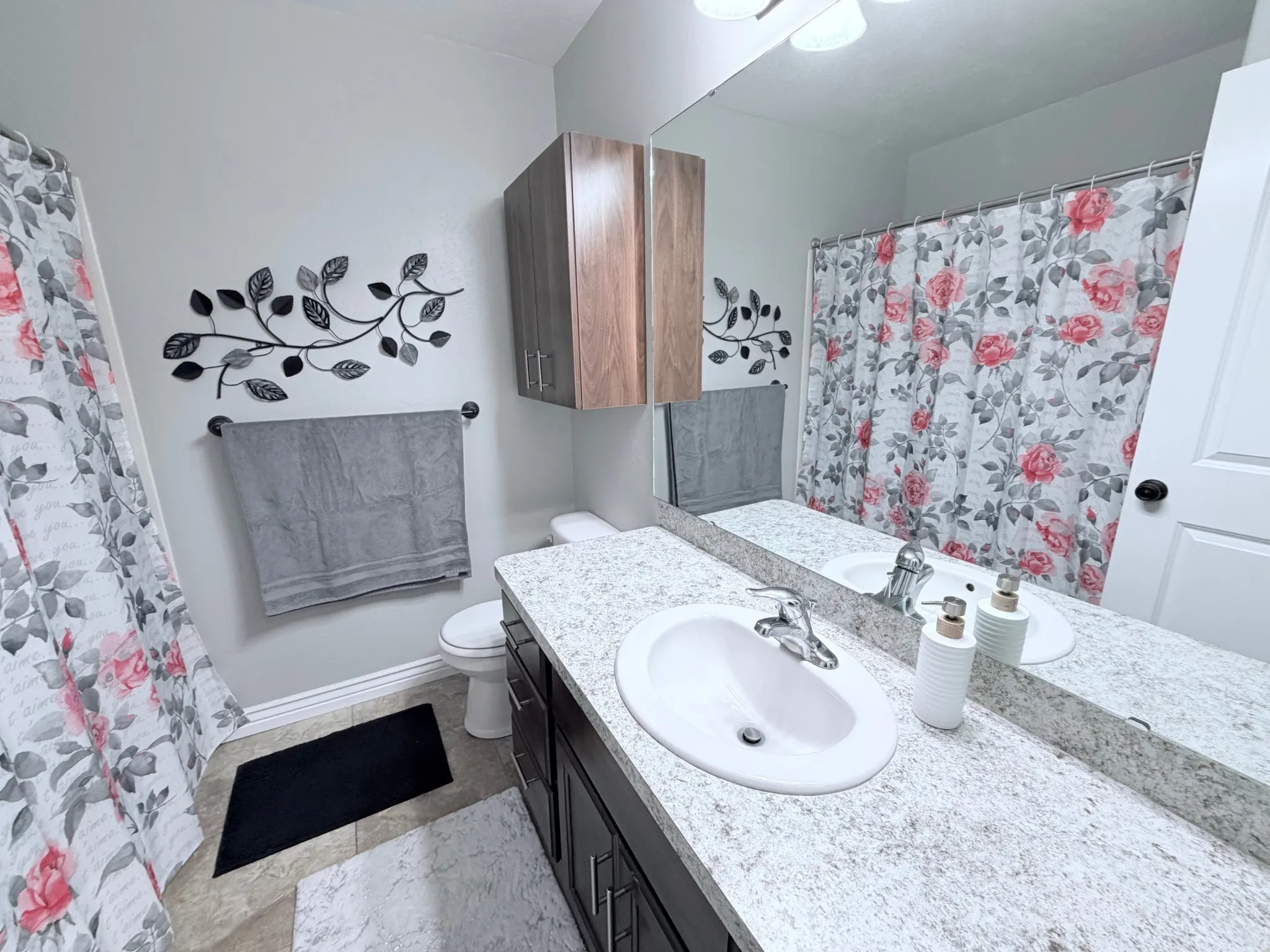 Bathroom #3 with a vanity featuring a white oval sink, light countertop, dark cabinetry and expansive wall-mounted mirror