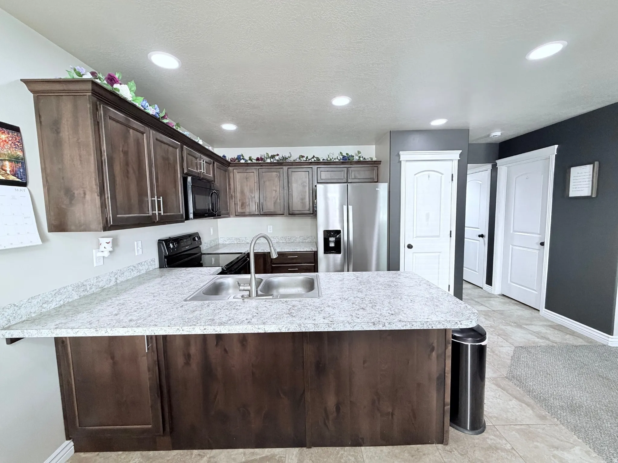 Kitchen featuring a large island with a double basin sink, dark wood-finish cabinetry, light countertops, and recessed ceiling lighting