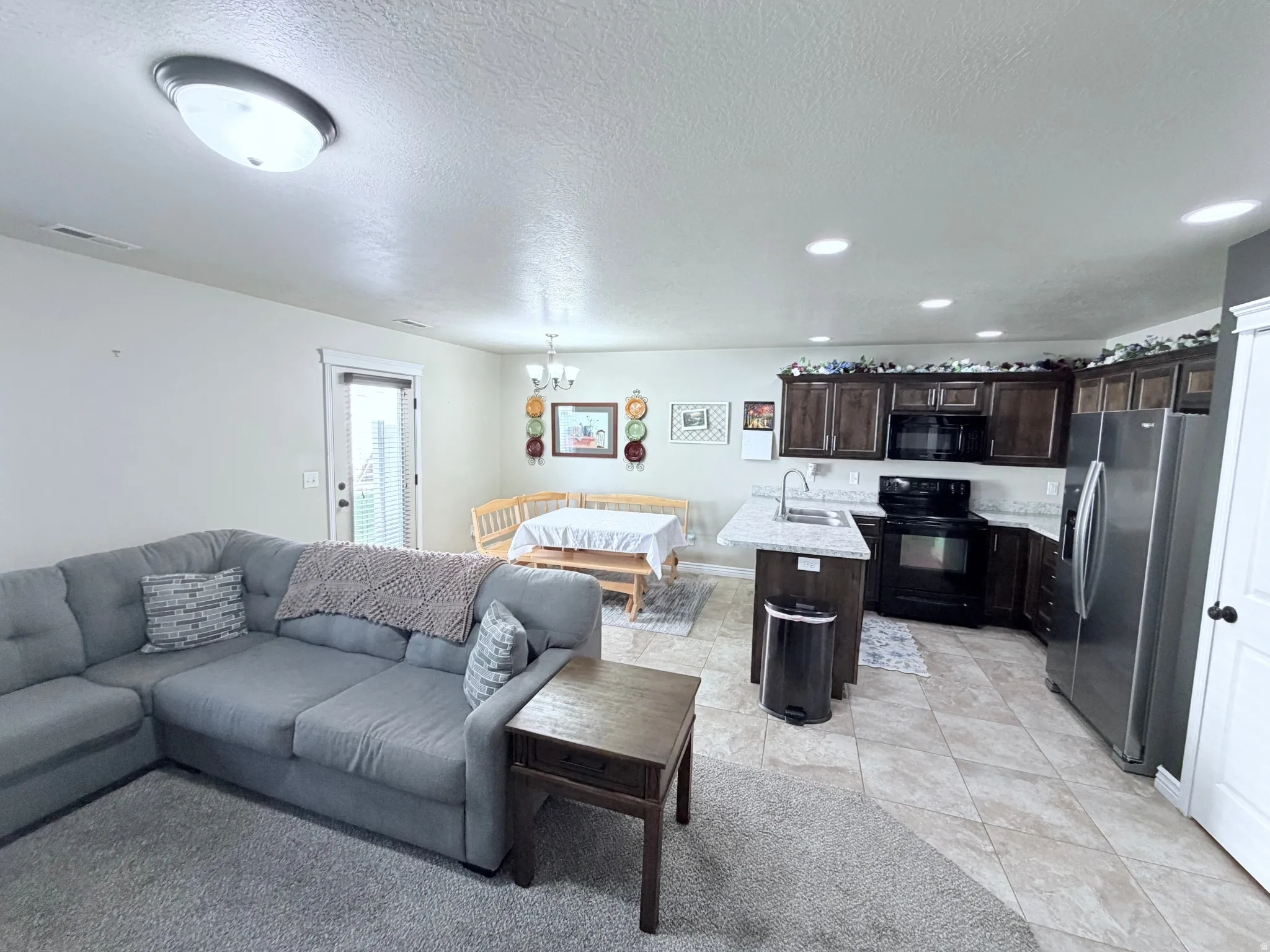 Open-concept living space featuring a kitchen with dark cabinetry, light-toned countertops, stainless steel appliances and an island