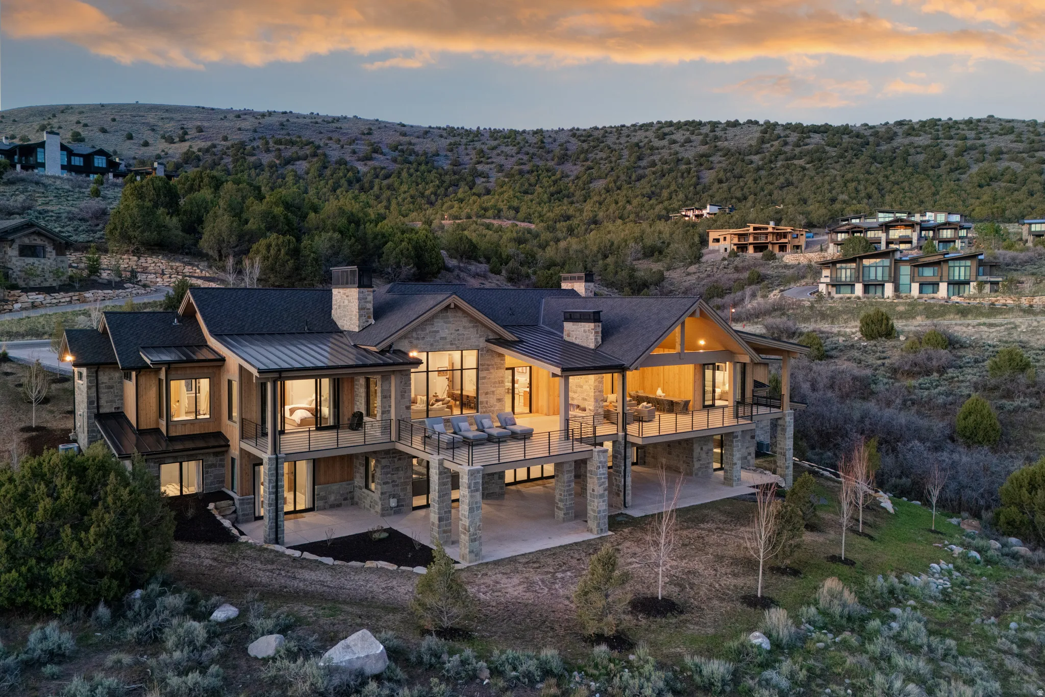 Contemporary mountain-style residence featuring extensive stone and wood siding, multiple expansive decks with glass railings, a stone chimney, and large windows throughout