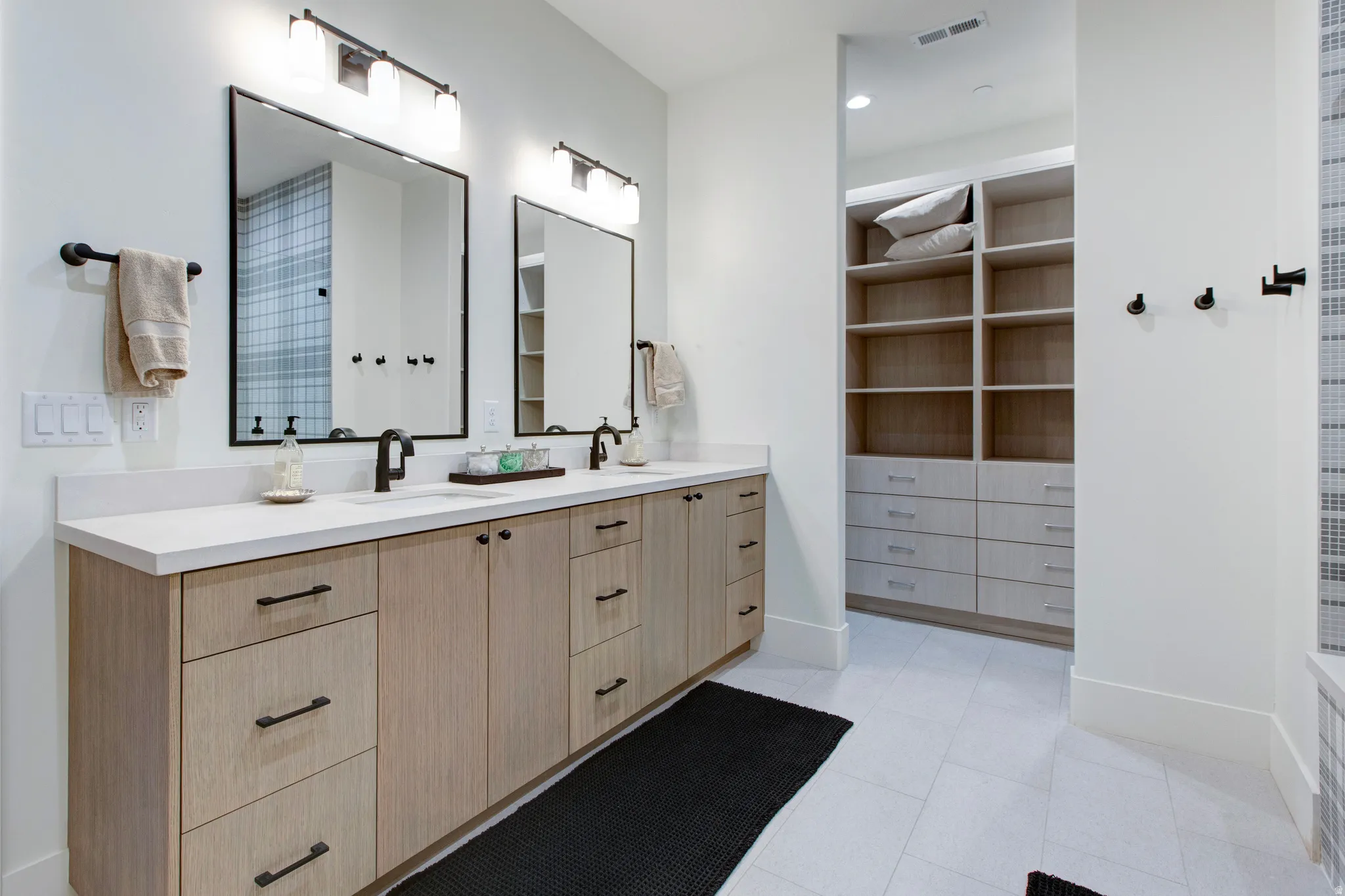 Dual vanity with light wood-finish cabinetry, white stone countertops, and matte black fixtures