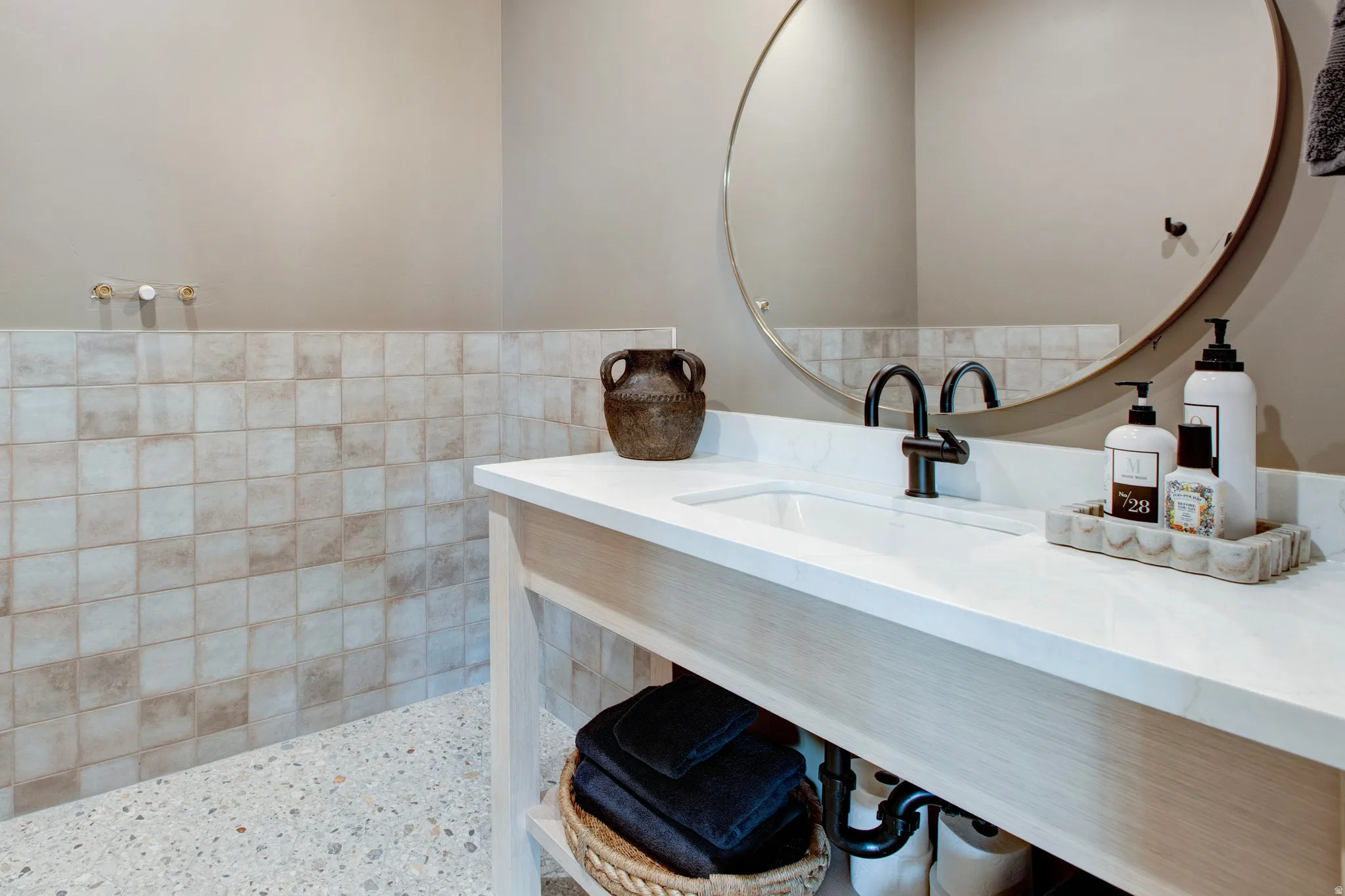 Bathroom vanity featuring a light wood-finish base with an integrated sink, white countertop, and matte black faucet
