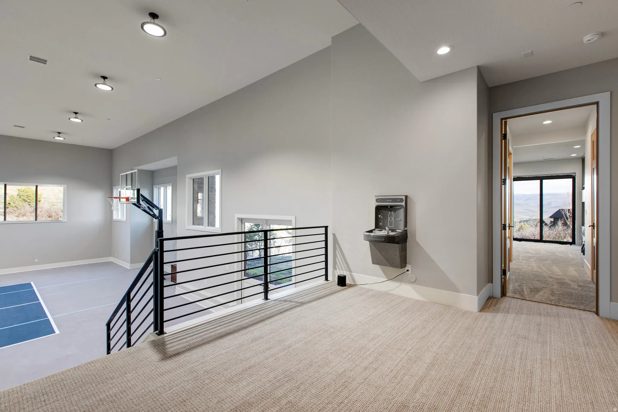 Upper-level landing featuring neutral carpeting, a built-in water dispenser, and a full-height doorway opening to a room with a sliding glass door