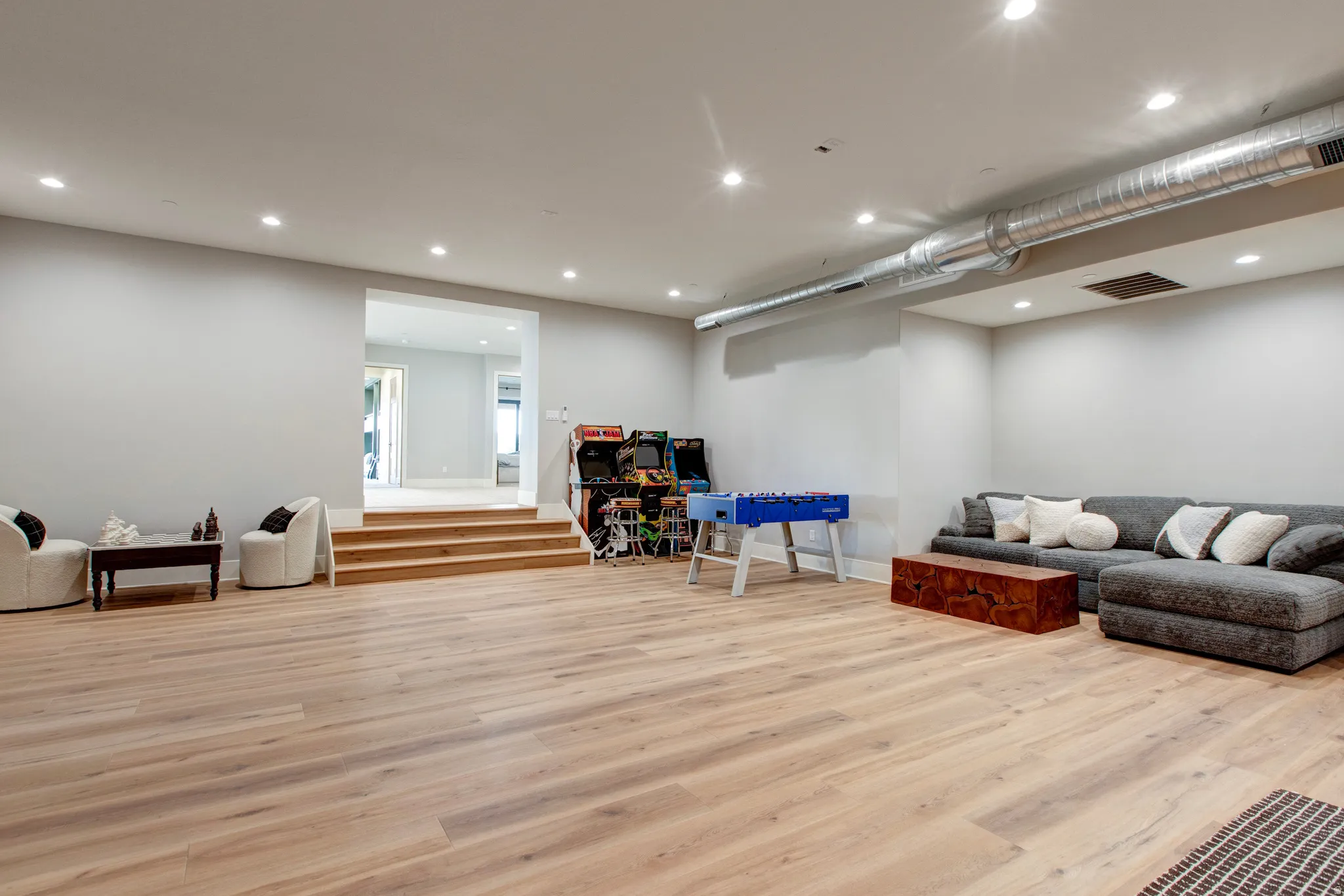 Expansive open-concept room featuring light wood-finish flooring, recessed ceiling lighting, and a prominent exposed metal ductwork system