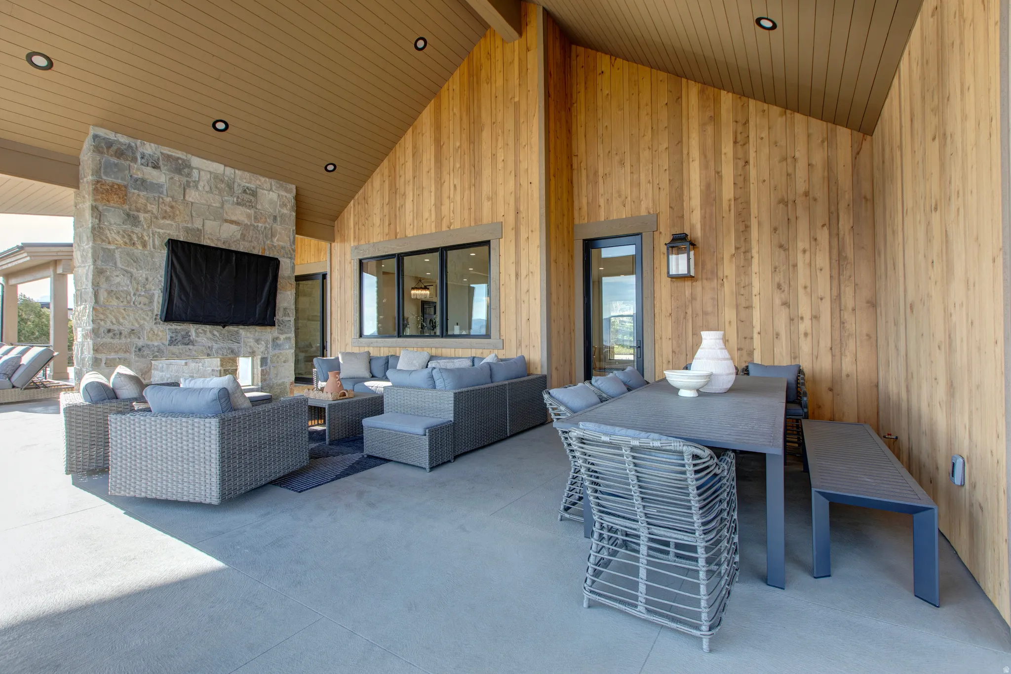 Expansive covered patio featuring a stone fireplace, wood paneling, recessed lighting, and a large multi-pane window