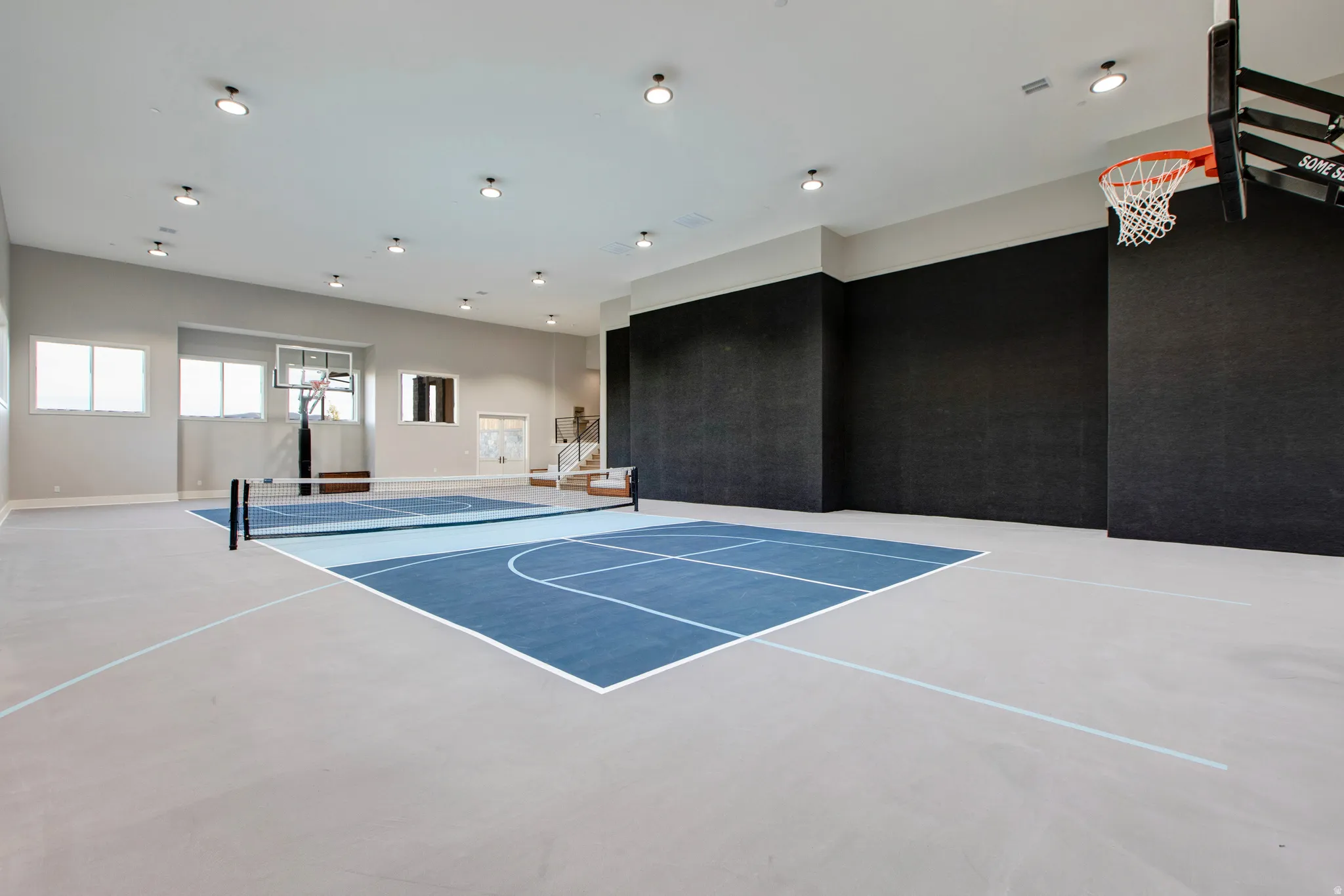 Indoor athletic court featuring a basketball hoop, a net for court sports, and perimeter striping on a light gray and blue surface