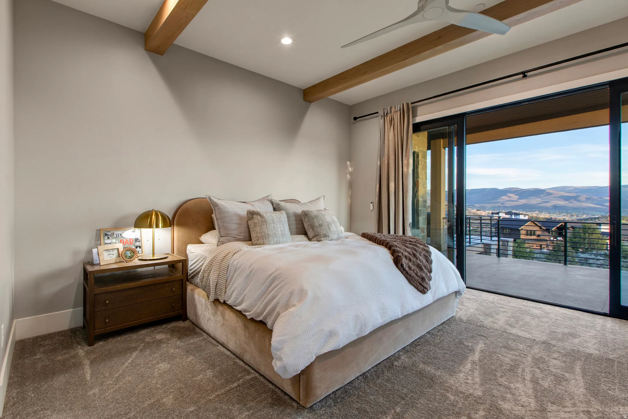 Carpeted room featuring exposed ceiling beams and a modern ceiling fan