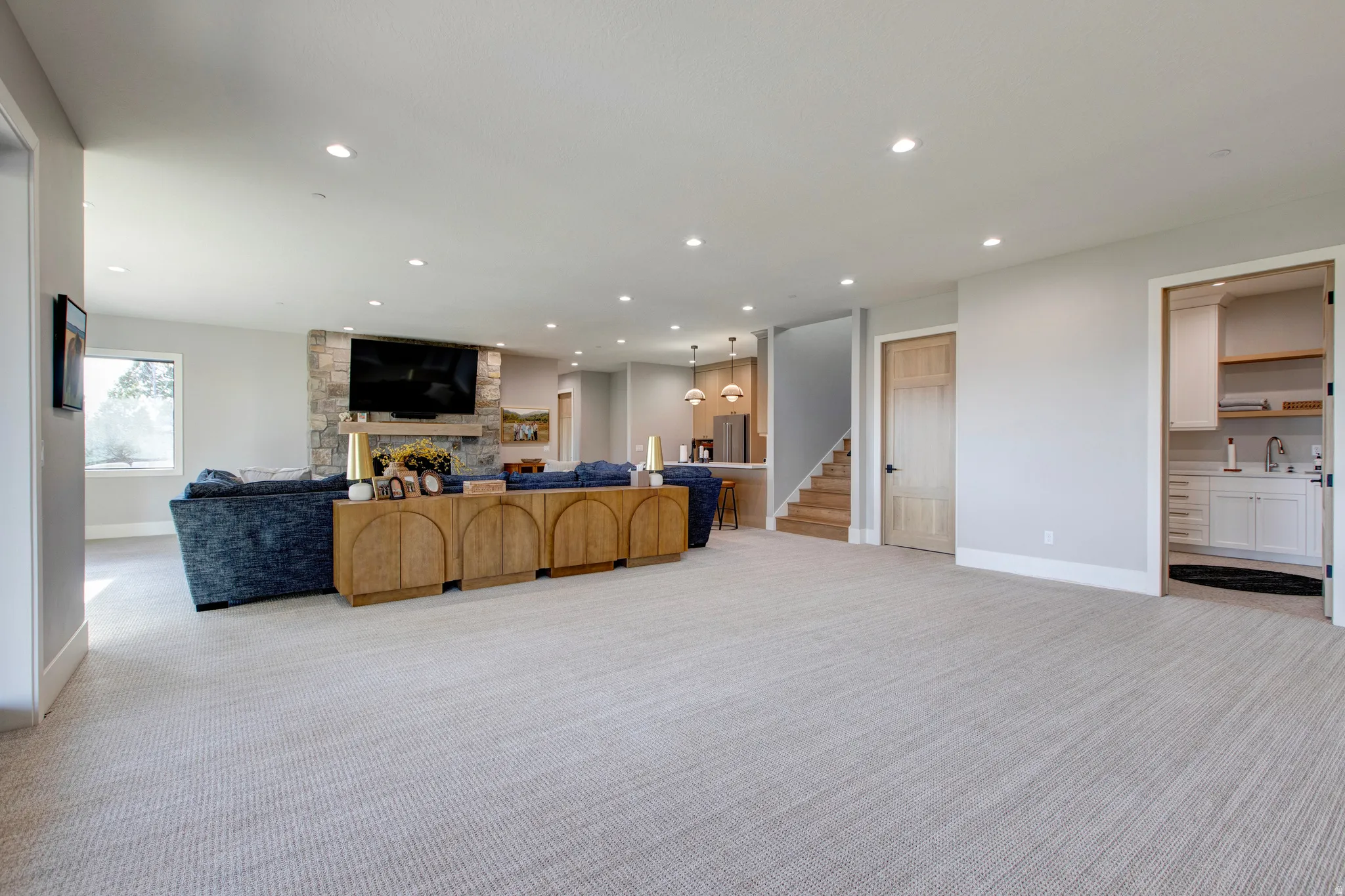 Expansive carpeted living area featuring recessed lighting, a stone-clad fireplace, and a built-in entertainment center