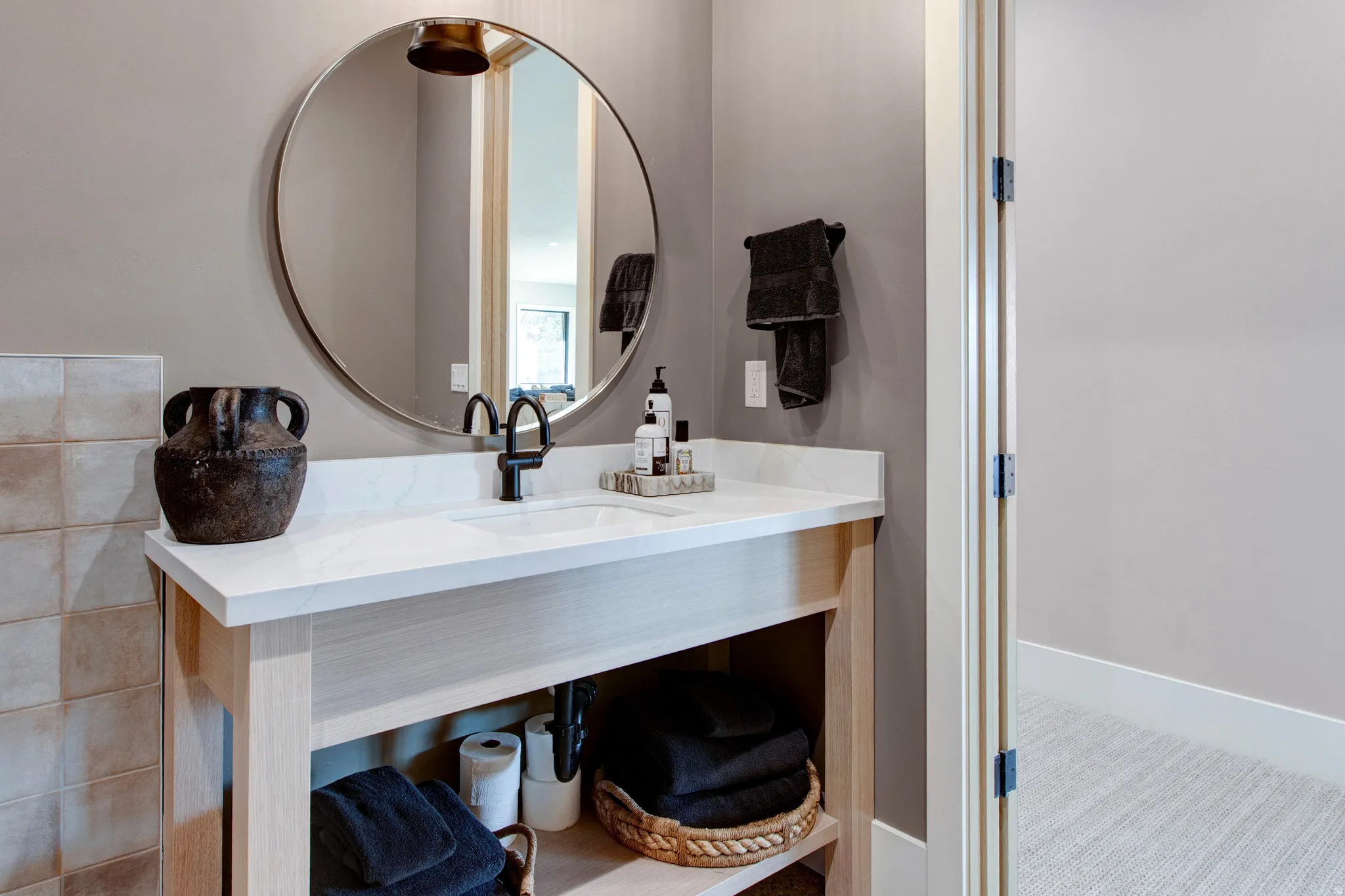 Bathroom vanity featuring a light wood-finish base, integrated white sink, and black matte faucet