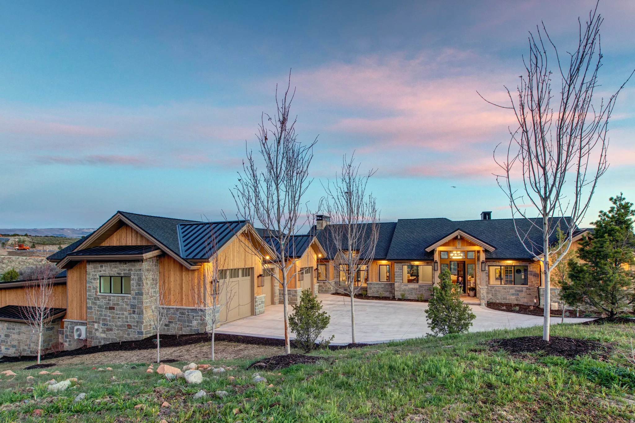 Stone and wood-sided residence featuring a multi-car garage, dark-toned roofing, and a prominent front entry with architectural details