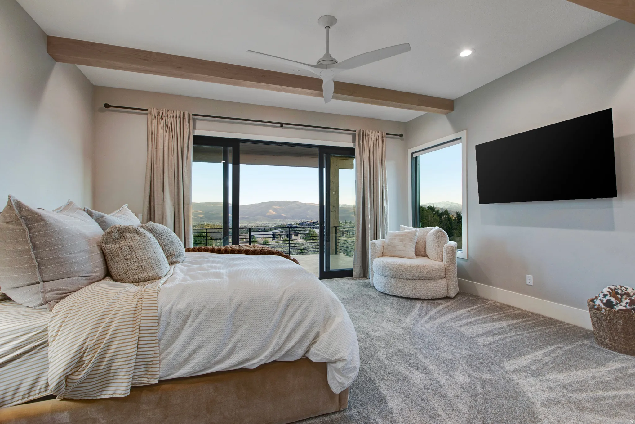 Expansive room featuring a large bed, tray ceiling with wood-finish beams, and a ceiling fan
