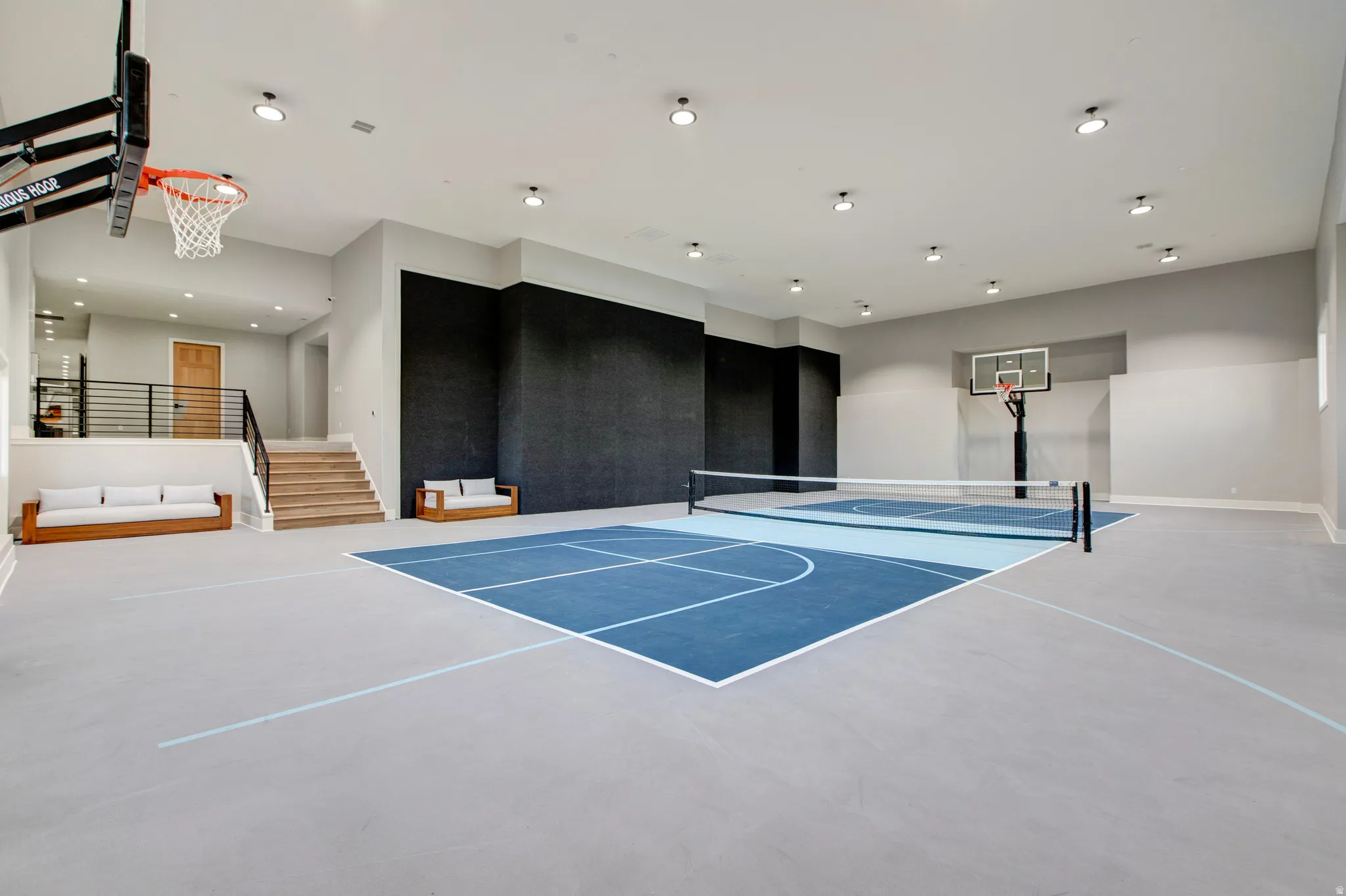 Indoor sports court featuring a painted blue and light grey surface, basketball hoops at opposing ends, and a net for court sports