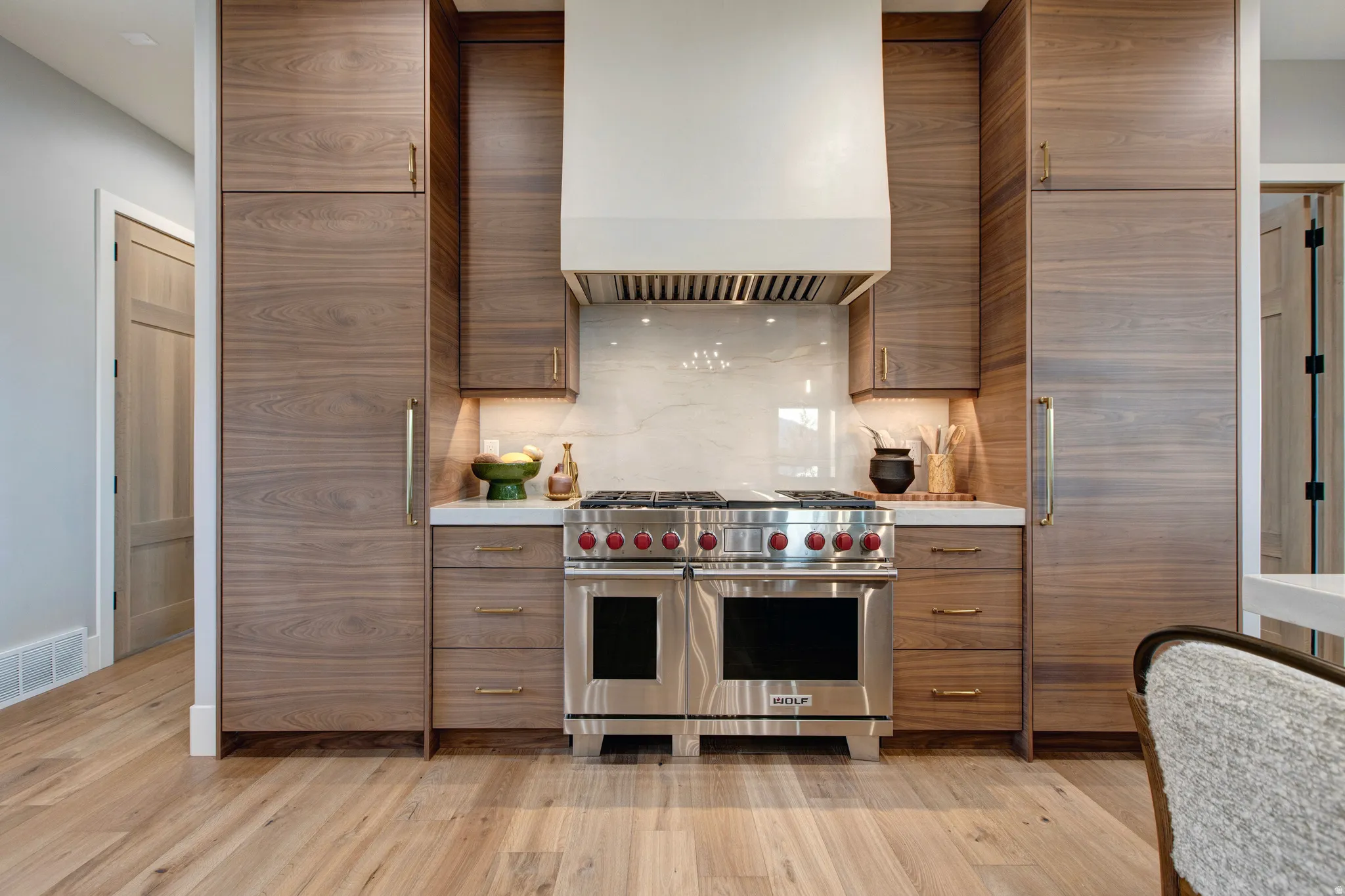 Gourmet kitchen featuring a stainless steel range with red knob accents, a white vent hood, integrated wood-finish cabinetry, a white countertop, and a light-colored backsplash